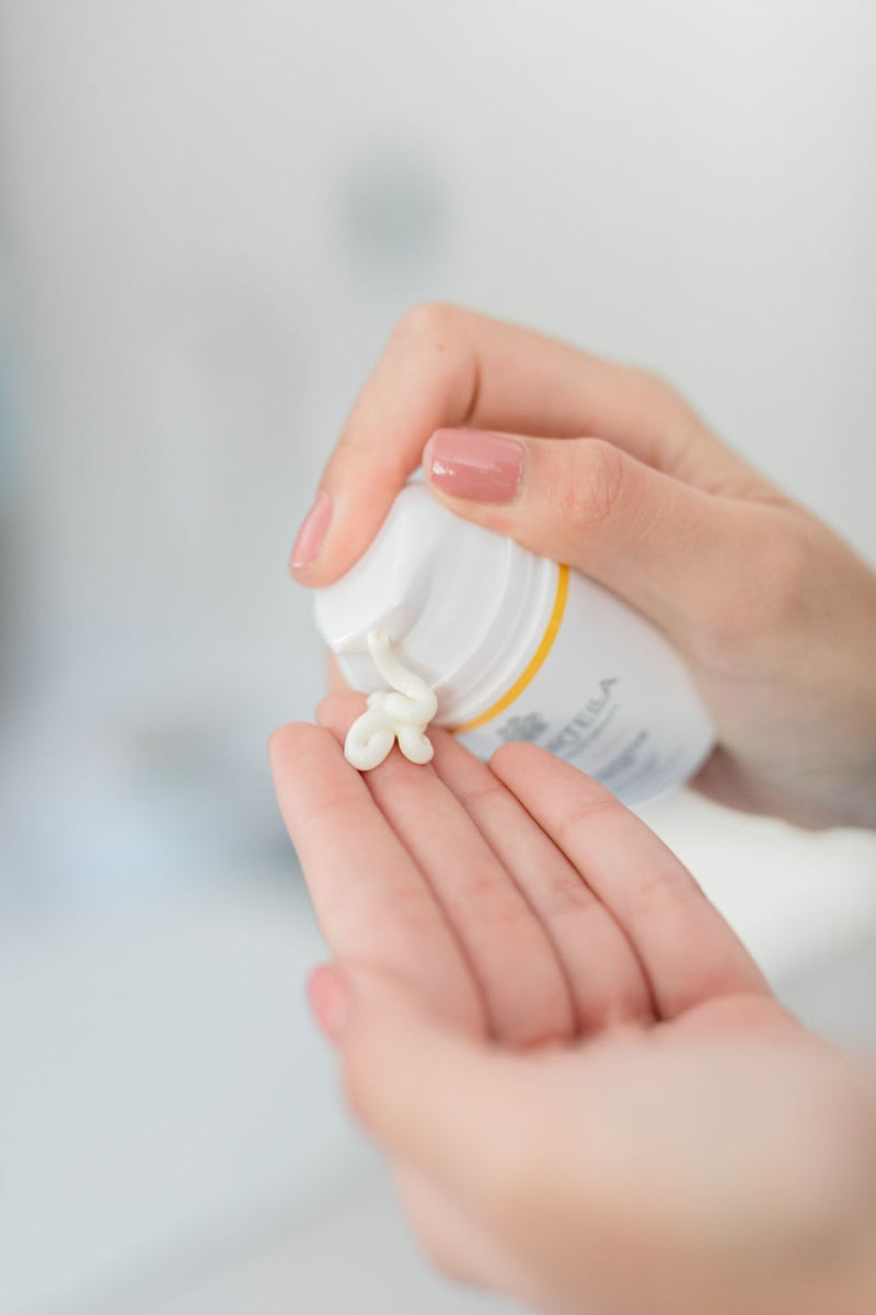 Close up of women’s hands pumping out immortelle face cream on forefinger.