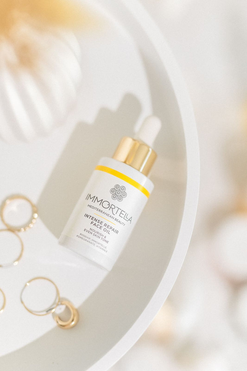 Natural, handmade immortelle facial oil, intensive anti-aging treatment. Close up of beautiful white bottle on side table, with golden jewelleries.