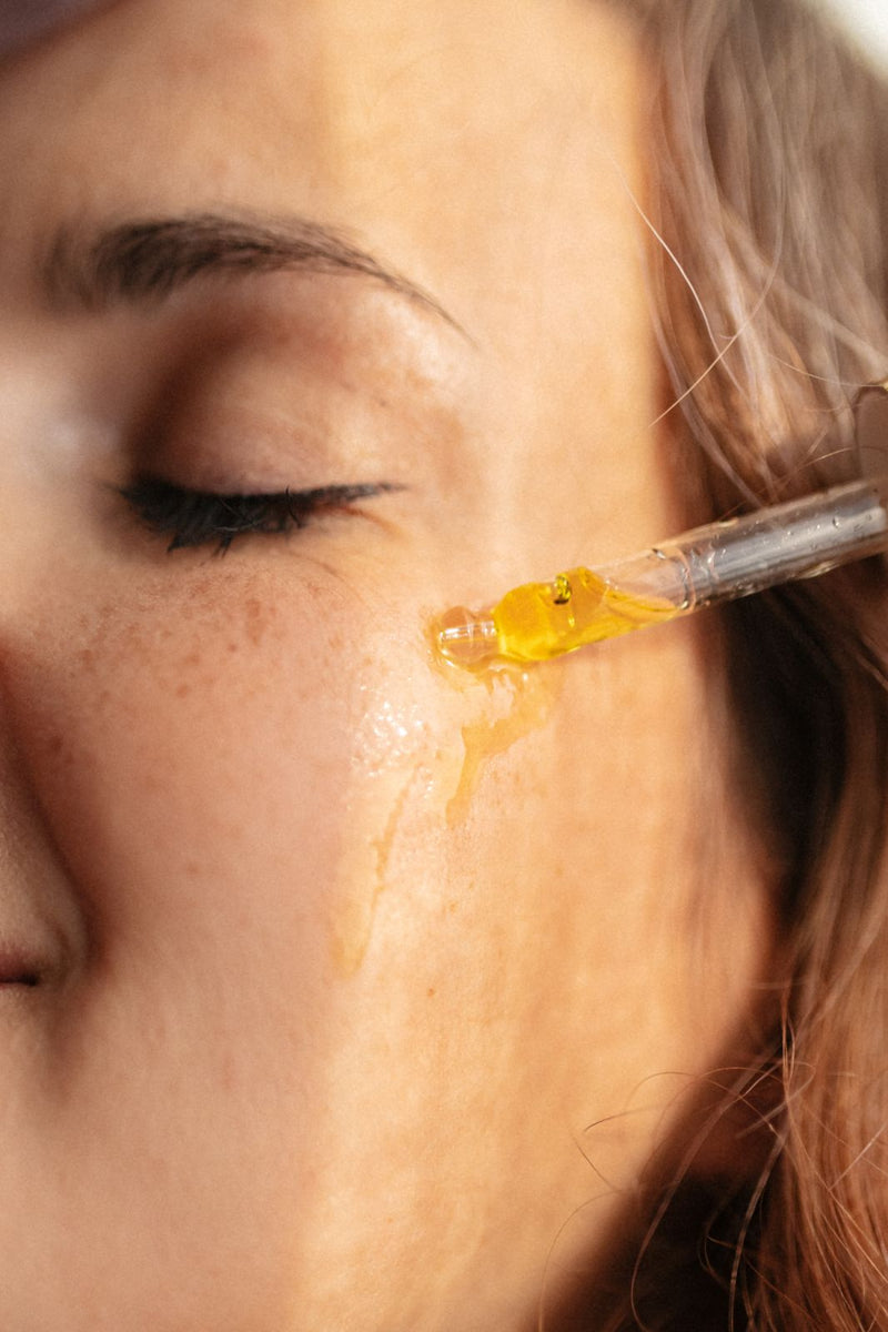 Close up of a beautiful young woman, who is applying immortelle oil on her face with dropper.