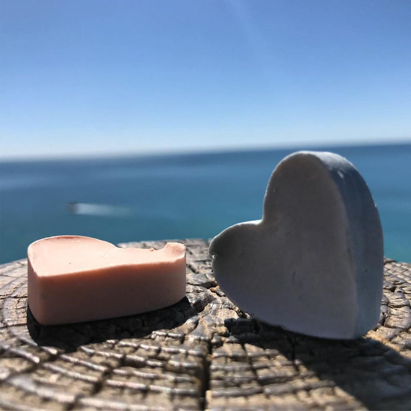 Close up of two little cute, natural handmade hart shaped soaps on the wooden board. Behind the orange, lemon and citronella soaps is beautiful blue Adriatic Sea during the summer time.