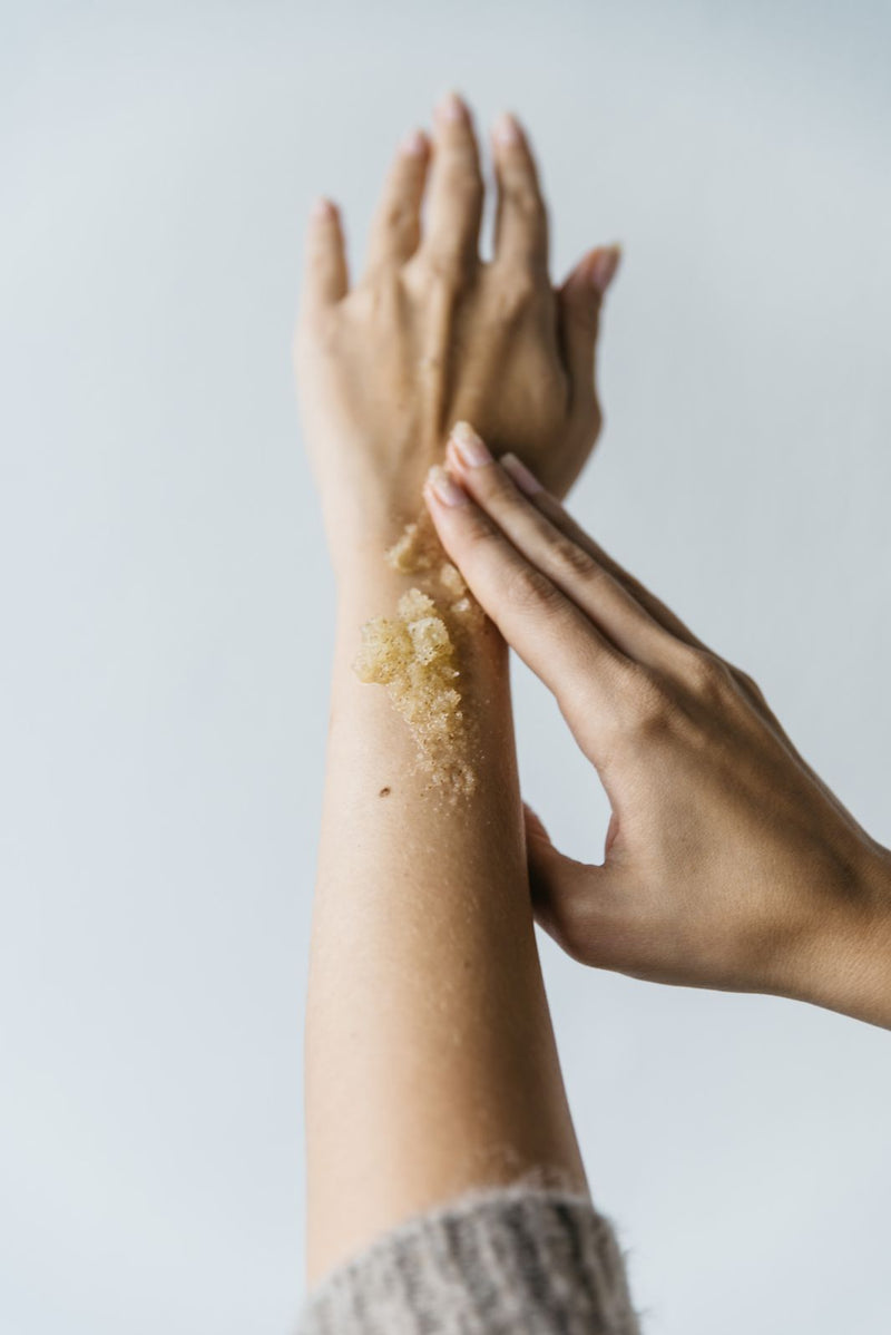 Close up of women’s hand applying natural handmade sea salt and citrus body scrub on her arm.