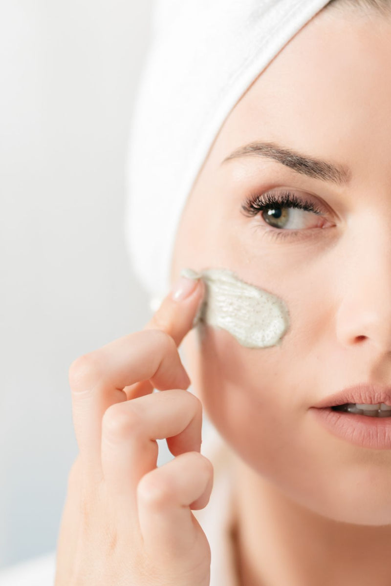 Close up of attractive young women, applying natural clay scrub and mask on her face.