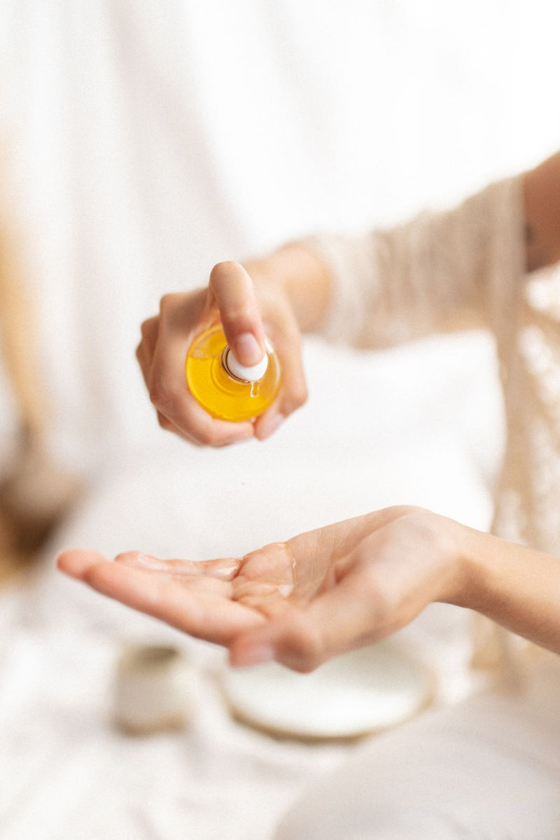 Close up of hands of young women pouring immortelle body oil in her hands. Natural dry golden body oil, specially designed for dry skin.