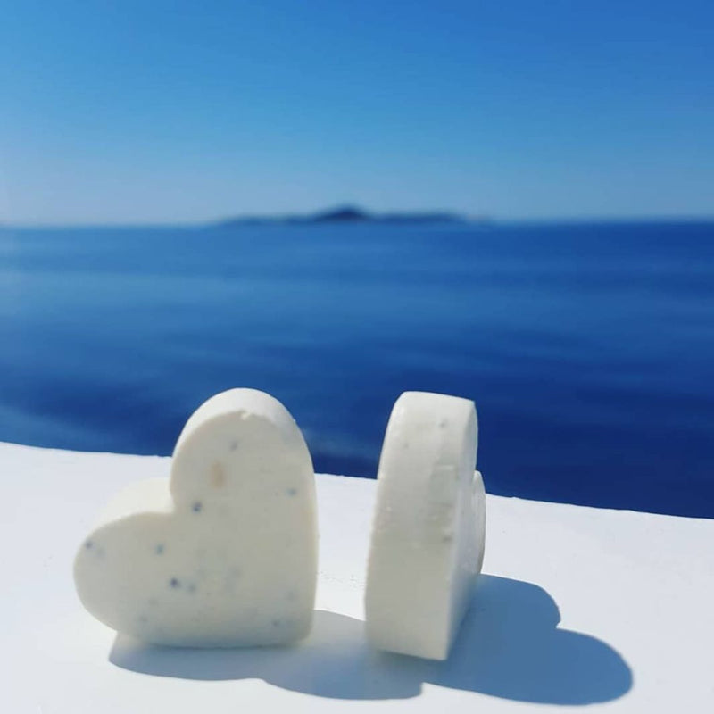 Close up of two little cute hart shaped soaps made of extra virgin Croatian olive oil, and pure mint, clove and cinnamon essential oils. Inside of natural soaps you can see the little poppy seeds. The soaps are lying on the white board, behind them is beautiful summery scenery of the blue Adriatic sea.