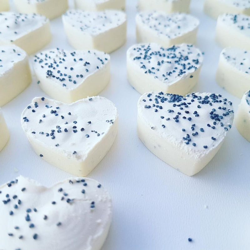 Close up of little cute hart shaped soaps made of extra virgin Croatian olive oil, and pure mint, clove and cinnamon essential oils. Inside of natural soaps you can see the little poppy seeds. The soaps are laying on the white board it the soapery.