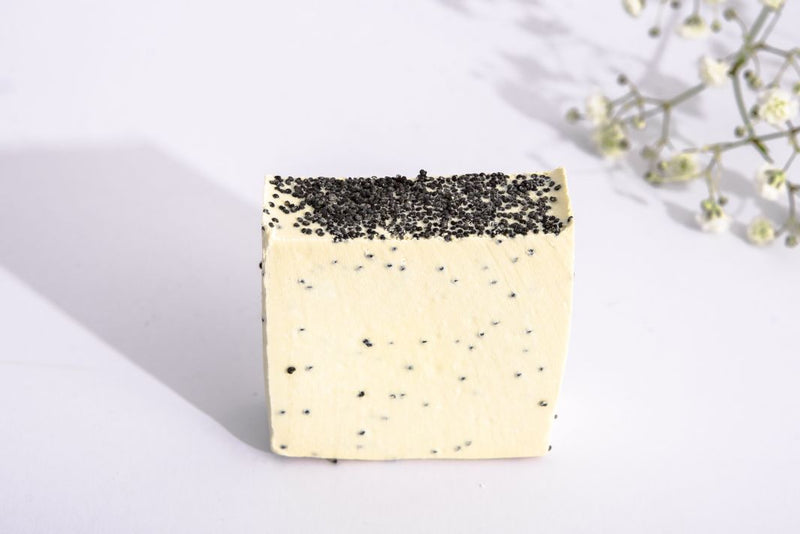 Close up of natural, handmade soap bar with poppy seeds on top and inside of the soap bar. Soap is made of extra virgin Croatian olive oil, and pure mint, clove and cinnamon essential oils. The soap is on the white background with beautiful white flowers.
