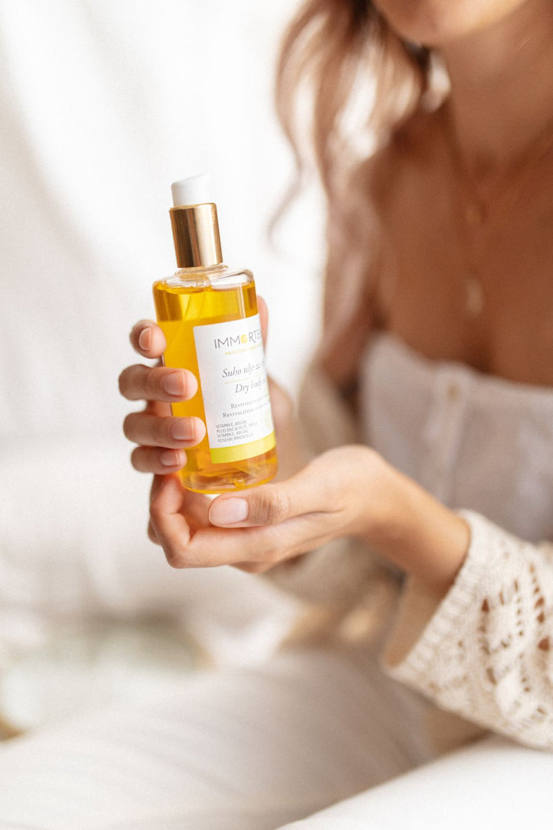 A beautiful young woman is holding in her hands immortelle dry body oil. Natural dry Body oil is suitable for all skin types - especially dray and dehydrated.