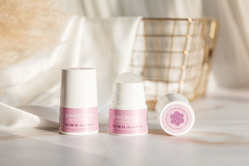 Three lavender roll-on products one next to each other. They are standing on beautiful marble desk; behind the roll-ones is white silk fabric and golden basket. 
